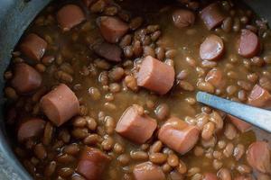 olla de cerdo y frijoles con trozos de hot dog cortados foto