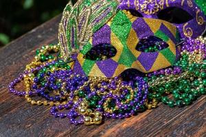 Mardi Gras color beads with masks on wooden table in sunlight photo