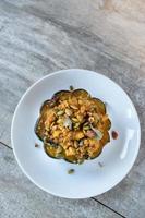 roasted acorn squash bowls filled with bread stuffing and herbs on white plate flat lay photo