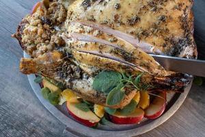 Whole baked herbed turkey with sides on round serving tray garnished with rosemary and sage flat lay