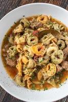 bowl of tortellini pasta soup with herbs flat lay photo