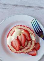 Serving of jelly roll cake slice with cream and fresh strawberry slices on plate flat lay photo