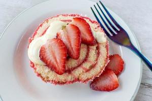 Serving of jelly roll cake slice with cream and fresh strawberry slices on plate flat lay photo