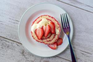 Serving of jelly roll cake slice with cream and fresh strawberry slices on plate flat lay photo