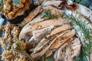 Serving tray of sliced roasted turkey with Thanksgiving sides and garnished with rosemary and sage photo