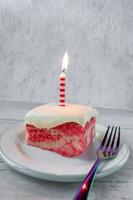 Slice of yellow jello cake with pudding frosting with a single lit candle on plate with fork photo