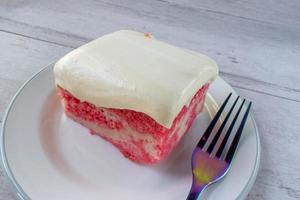 Slice of yellow jello cake with pudding frosting on plate with fork photo