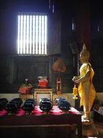 Standing gold buddha in the wooden old temple with lots of alms bowl photo