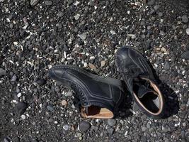 A pair of new black color boots shoes on the black rock beach photo