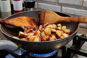 Frying pan with fried potatoes and wooden spatulas on gas stove. Step by step recipe photo
