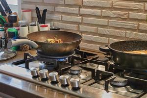 Frying pans with fried potatoes, chestnuts, parsley, parmesan on gas stove in the kitchen. Step by step recipe photo