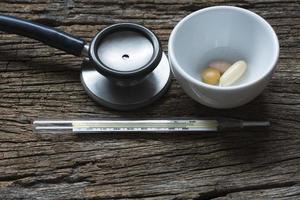 Medications in a cup, thermometer and stethoscope photo