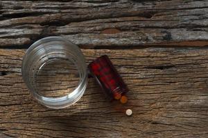 Medication, a plastic bottle and a glass of water on wooden background photo