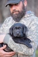 Man in military clothes with a Labrador Retriever puppy in his arms. Man and dog. photo