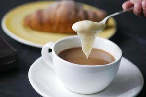 pouring condensed milk in cup of tea photo