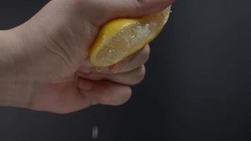 Hand squeezing half of lemon with lime drop on black background. video