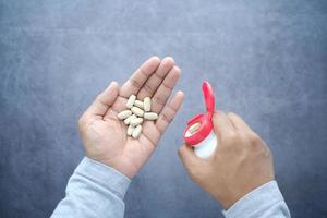 La mano del hombre con la medicina derramada fuera del contenedor de pastillas foto