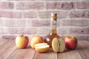 Vinagre de manzana en botella de vidrio con manzana verde fresca en la mesa foto