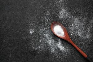 spoon of white sweetener on a black background . photo