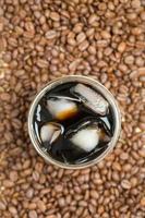 Coffee cup of iced americano on table in Roasted coffee beans textured background. top view Black coffee with space for text photo