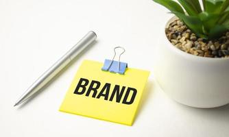 White notepad with text Brand lying on laptop on wooden table. Marketing business concept photo