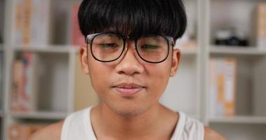 Nahaufnahme des Gesichts einer asiatischen Teenager-Mann-Brille, die in der Wohnung lächelt und in die Kamera schaut. süßer Teenager-Student zu Hause. Lifestyle- und People-Konzept.