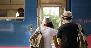jong aziatisch reizigerspaar stapt op de trein op het treinstation. man en vrouw die beschermende maskers dragen, tijdens covid-19-noodsituatie. transport, reizen en social distancing concept.