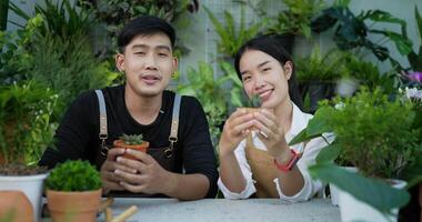 Portrait of a happy young asian couple gardener selling online on social media and looking at camera in the garden. Man and woman video call. Home greenery, selling online and hobby concept