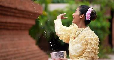 prise de vue à la main, belle jeune femme en costume traditionnel thaïlandais profiter des éclaboussures d'eau dans le temple lors du festival de songkran. nouvel an thaïlandais, culture thaïlandaise avec festival de l'eau video