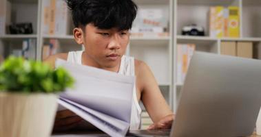 portrait d'un homme asiatique fatigué en singulet utilisant un ordinateur portable et regardant un document à la maison. homme endormi travaillant à la maison, pensant et se sentant pensif. travail à domicile surchargé la nuit dans la nouvelle normalité.