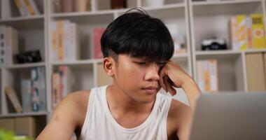portret van vermoeide aziatische man in hemd werkt op laptop terwijl hij thuis zit. slaperige man freelancer voelt zich aan het bureau. thuiswerken 's nachts overbelast in het nieuwe normaal. video