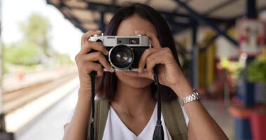 primer plano de una joven viajera asiática tomando una foto en cámara en la estación de tren. mujer mirando a la cámara. concepto de transporte, vacaciones y viajes. video