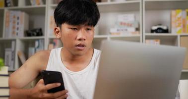 portrait d'un homme asiatique fatigué en singulet utilisant un smartphone et un ordinateur portable à la maison. homme endormi travaillant à la maison, pensant et se sentant pensif. travail à domicile surchargé la nuit dans la nouvelle normalité.