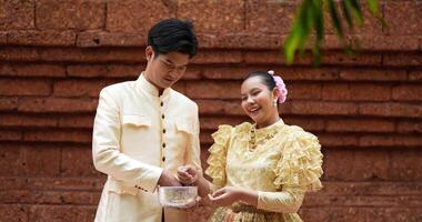 colpo a mano, la giovane coppia in costume tradizionale tailandese si diverte a spruzzare acqua nel tempio durante il festival di Songkran. capodanno tailandese, cultura tailandese con festival dell'acqua video