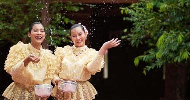 Handaufnahme, Vorderansicht, junge schöne Frauen mit traditioneller thailändischer Tracht haben Spaß daran, Wasser im Tempel auf dem Songkran-Festival zu spritzen. thailändisches neujahr, thailändische kultur mit wasserfest video