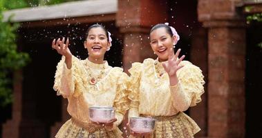 Handheld shot, front view, Young beautiful women with Thai Traditional costume enjoy to splashing water in the temple on Songkran festival. Thai New Year, Thailand culture with Water festival