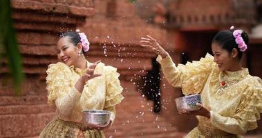 uit de hand geschoten, vooraanzicht, jonge mooie vrouwen met thais traditioneel kostuum hebben plezier met opspattend water in de tempel op songkran-festival. thais nieuwjaar, thailandcultuur met waterfestival video
