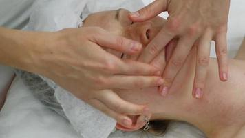 un masajista le da a una mujer un masaje facial profesional. la sala de masajes realiza un procedimiento de rejuvenecimiento. material de archivo full hd de alta calidad video