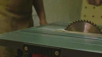 A mature man removes sawdust from a circular saw machine and prepares it for work