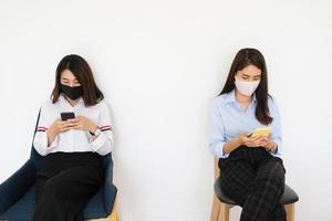 concepto de distanciamiento social, dos mujeres que usan máscaras y se distancian mientras están sentadas en teléfonos móviles siguiendo la tendencia social del coronavirus. foto