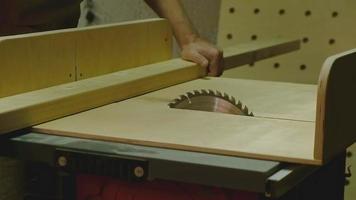 The master is a mature man holding a board with his hand sawing it on a circular saw machine