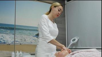 een masseur geeft een vrouw een professionele gezichtsmassage. de massageruimte voert een verjongingsprocedure uit. hoge kwaliteit full hd-beelden