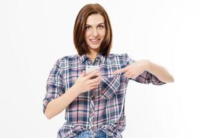 Smiling girl is pointing on smartphone standing on white background.Happy beautiful young woman holding mobile phone and pointing finger. photo