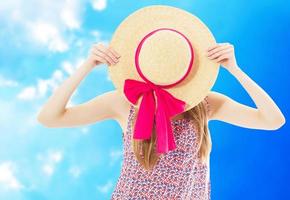 jovencita ocultar la cara detrás del sombrero de verano sobre fondo de cielo azul foto