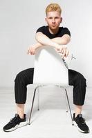 Young man on a chair, Portrait of handsome young man sitting on a chair, Proud and satisfied young man sitting on chair and looking at camera isolated, Casual young man in glasses photo