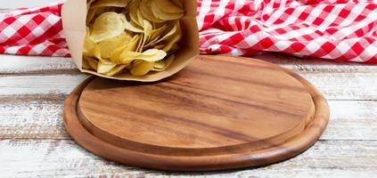 spicy red chilli potato chips and empty board on a wooden table photo