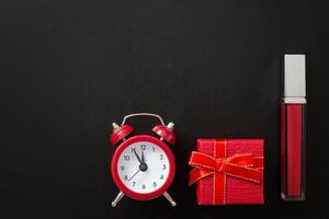 Lipstick cosmetic product with gift box and alarm clock isolated on black background. Sale time. Copy space. Top view photo