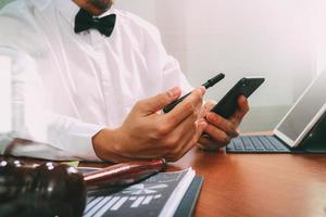 contexto de justicia y derecho. abogado masculino que trabaja a mano con teléfono inteligente, teclado de acoplamiento de tableta digital con mazo y documento en mesa de madera, efecto de filtro foto