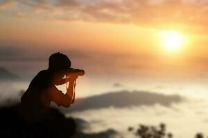 silueta de fotógrafo tomando fotos de una puesta de sol en las montañas.