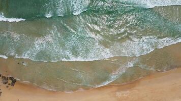 vista aérea de la playa de arena blanca y la textura de la superficie del agua. olas espumosas con cielo. hermosa playa tropical. increíble costa de arena con olas de mar blanco. concepto de naturaleza, paisaje marino y verano. video